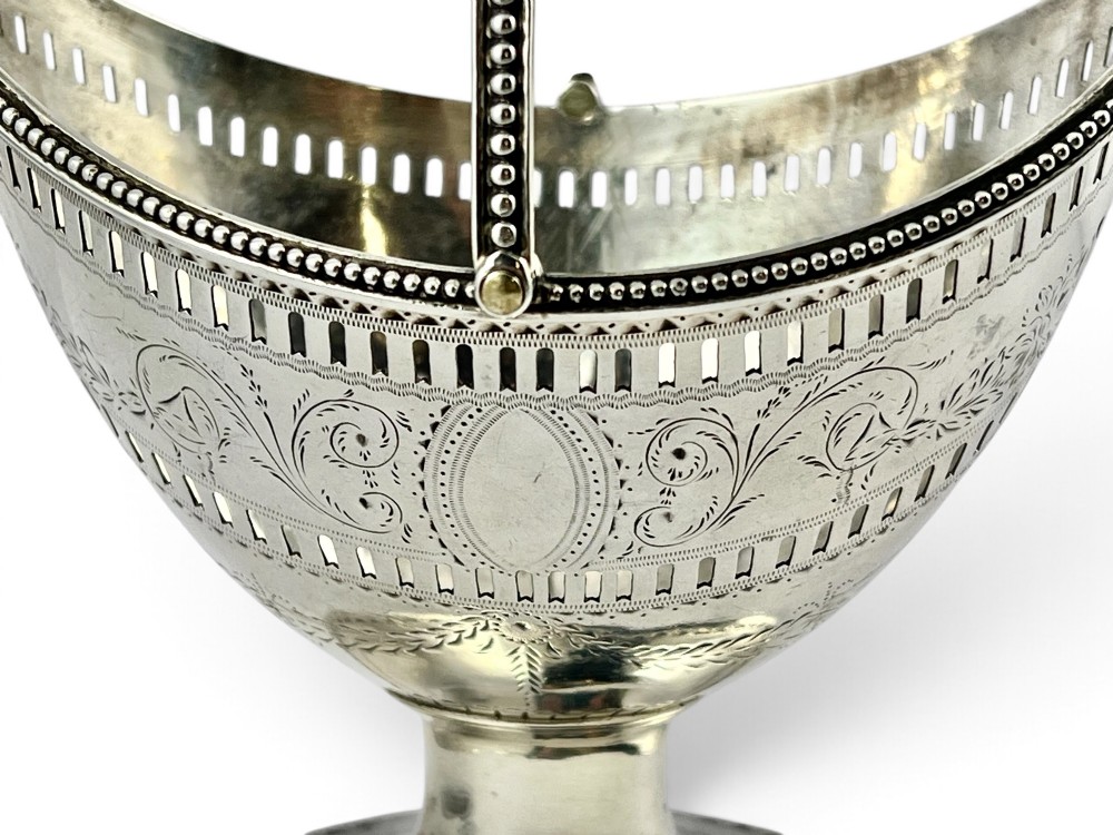 A George III sterling silver sugar basket featuring pierced geometric engraving, a beaded swing handle, a pedestal base, and a fitted cobalt blue glass liner. View X