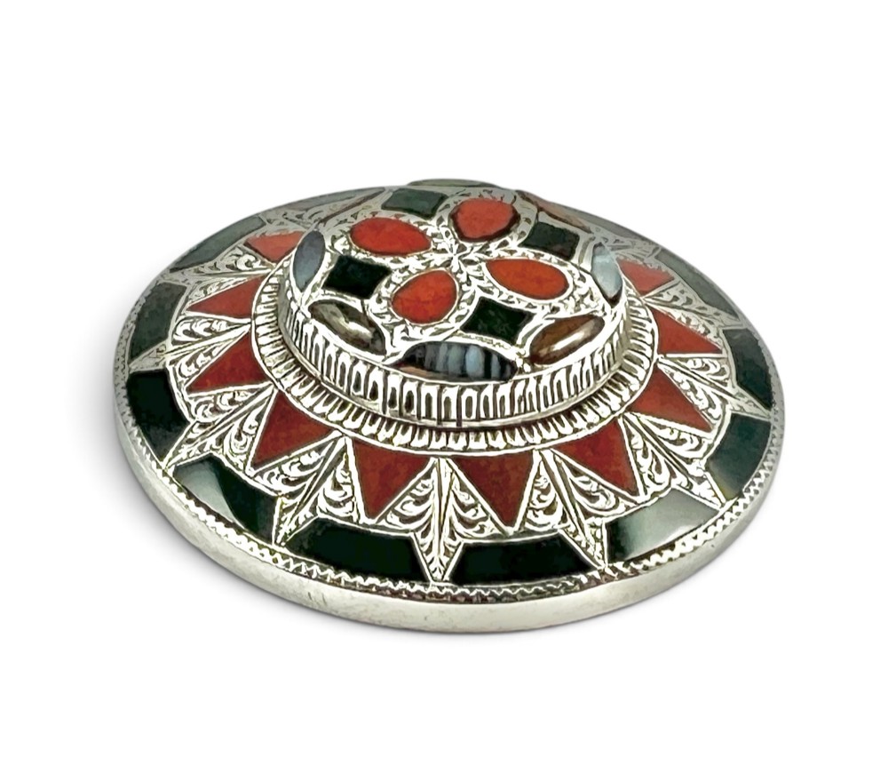 A circular Victorian Scottish silver brooch inlaid with geometric red carnelian, green jasper, and agate stones surrounding a central quatrefoil motif. View II