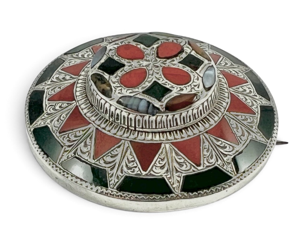 A circular Victorian Scottish silver brooch inlaid with geometric red carnelian, green jasper, and agate stones surrounding a central quatrefoil motif. View VI