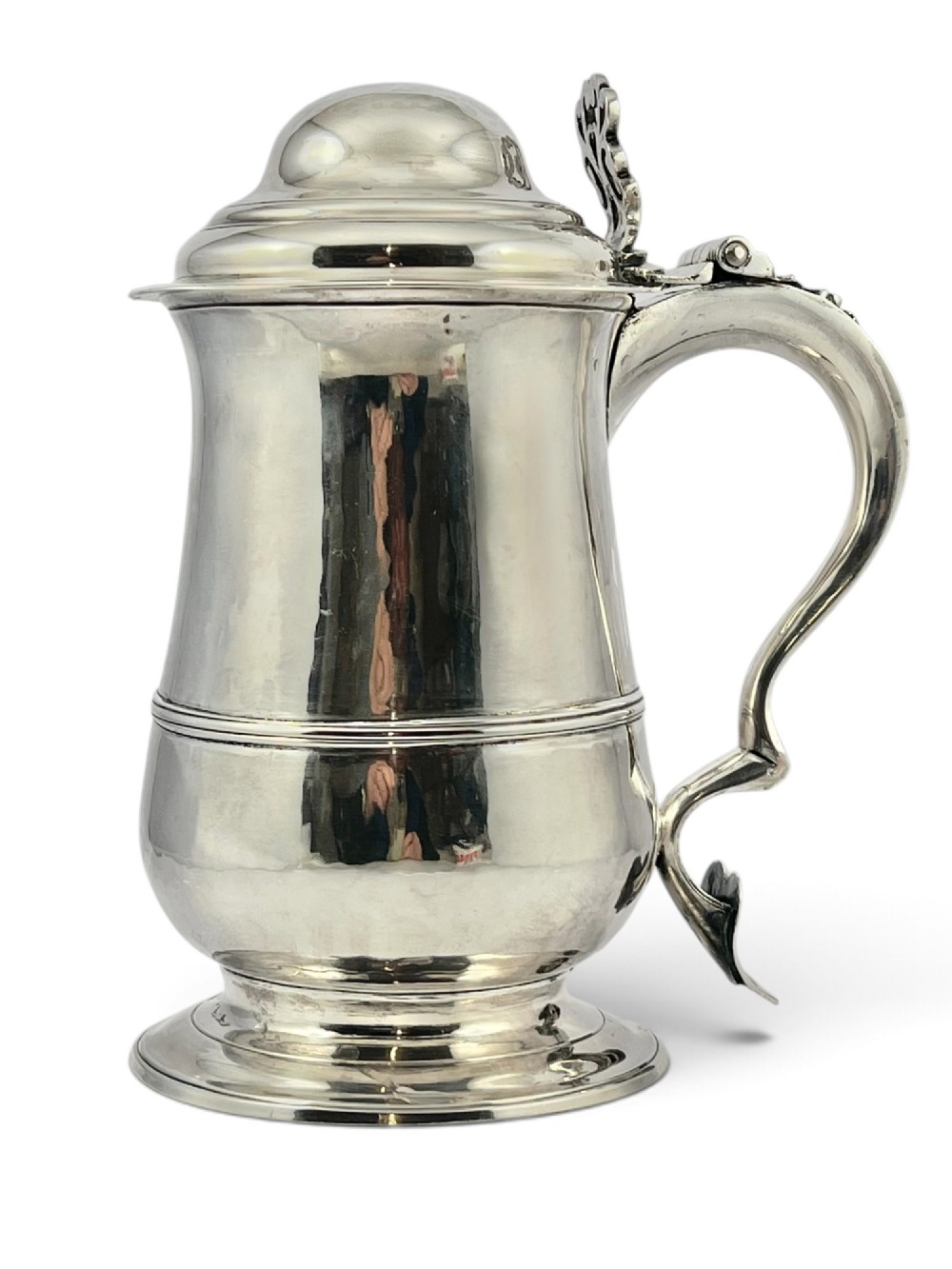 A George III sterling silver lidded tankard featuring a tapered body with a central mid-rib, a hinged domed lid, a pierced thumbpiece, and a double-scroll handle.