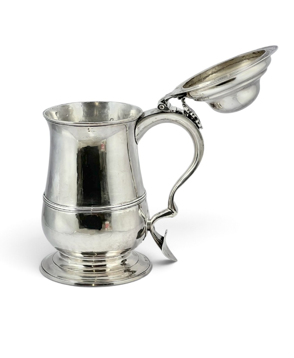 A George III sterling silver lidded tankard featuring a tapered body with a central mid-rib, a hinged domed lid, a pierced thumbpiece, and a double-scroll handle. View IV