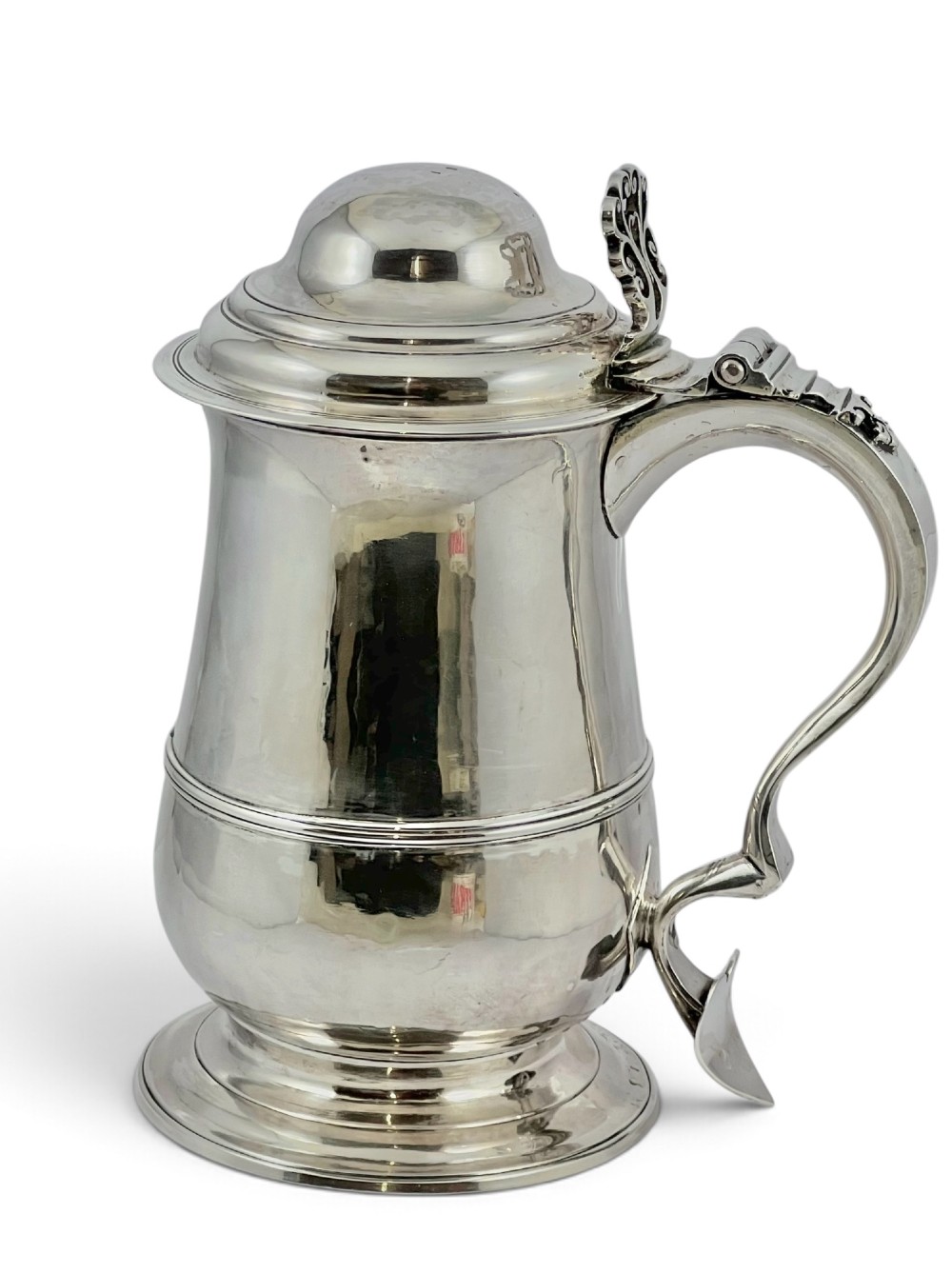 A George III sterling silver lidded tankard featuring a tapered body with a central mid-rib, a hinged domed lid, a pierced thumbpiece, and a double-scroll handle. View V