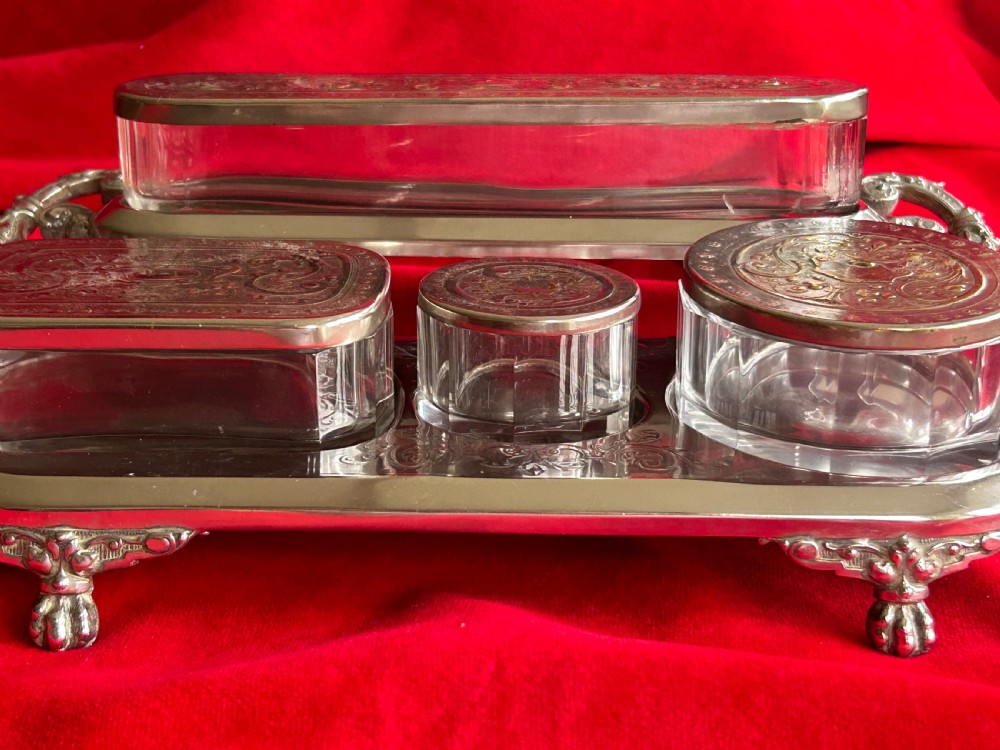 A tiered silver-plated metal stand by WMF holding four clear cut-glass pots with relief-patterned lids resting on ornate feet. View II