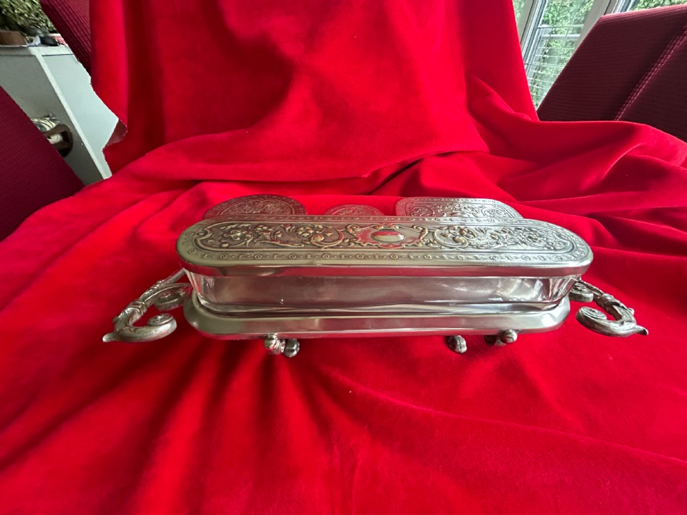 A tiered silver-plated metal stand by WMF holding four clear cut-glass pots with relief-patterned lids resting on ornate feet. View X