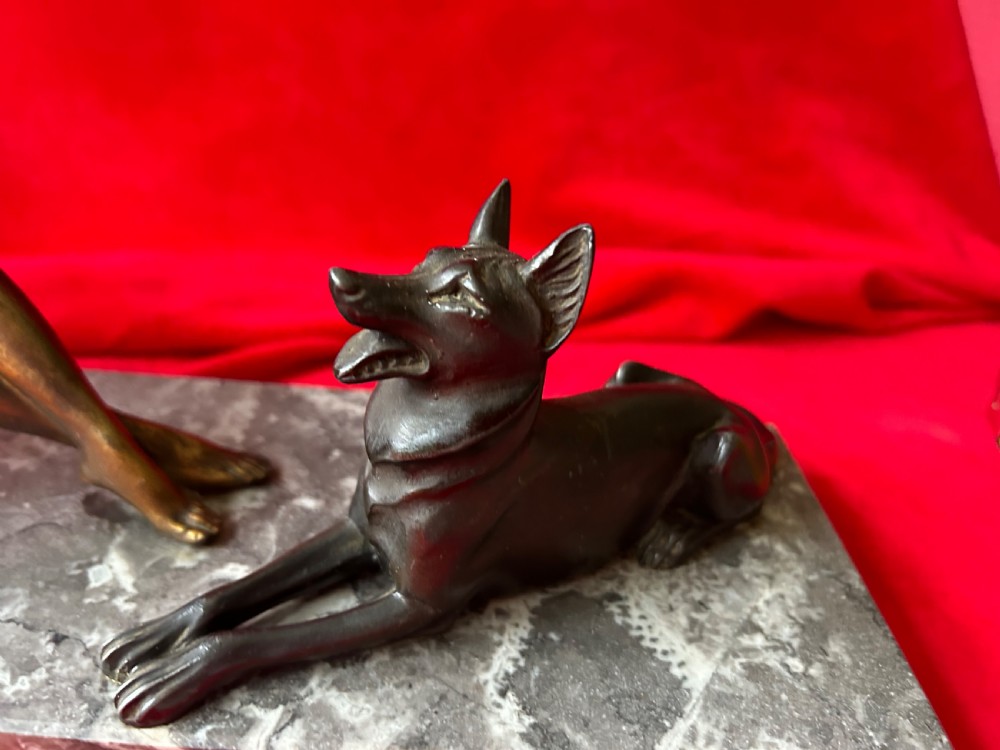 An Art Deco bronze figure group depicting a reclining stylized woman holding an orb beside a seated dog, set on a grey marble plinth. View II