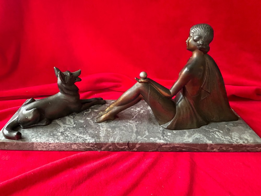 An Art Deco bronze figure group depicting a reclining stylized woman holding an orb beside a seated dog, set on a grey marble plinth. View V