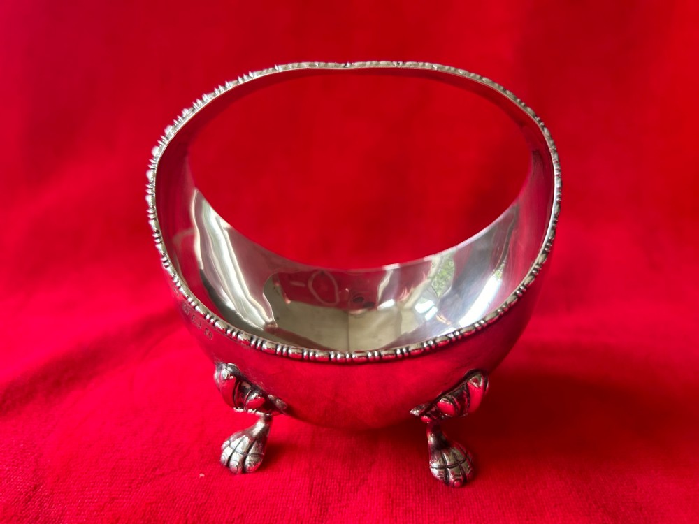 A polished silver bonbon dish with a high overhead handle, beaded rim, and claw feet.