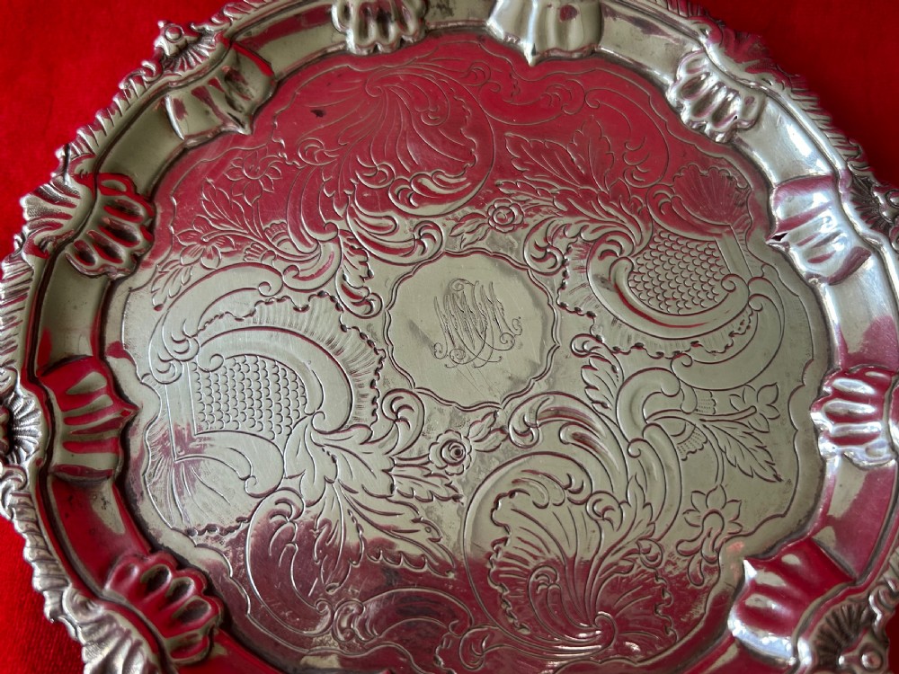 A circular George III sterling silver card tray featuring a shell and scroll cast rim with intricate hand-engraved foliate ornamentation on the flat surface. View III