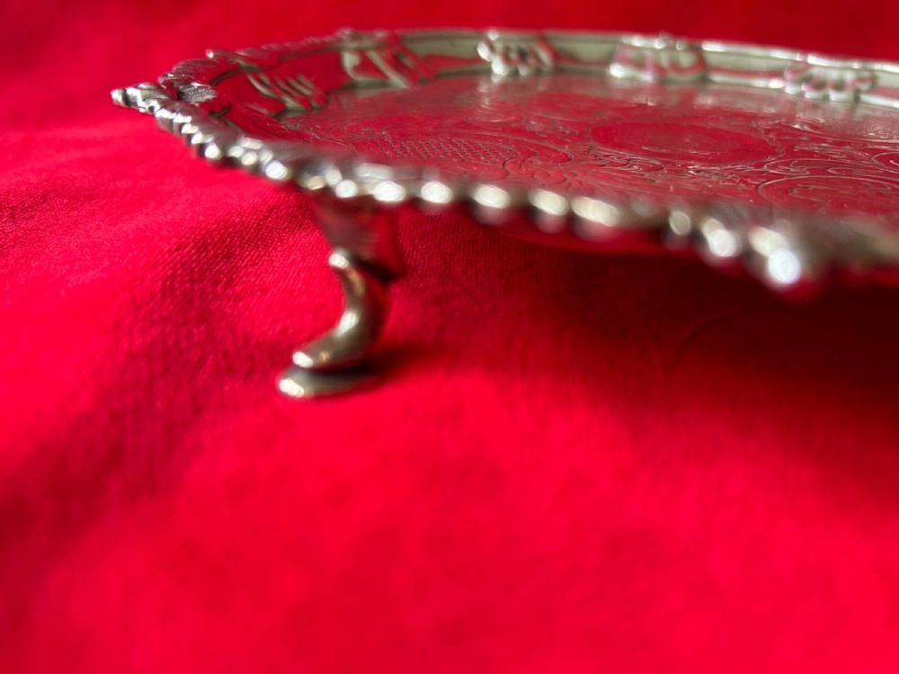 A circular George III sterling silver card tray featuring a shell and scroll cast rim with intricate hand-engraved foliate ornamentation on the flat surface. View IV