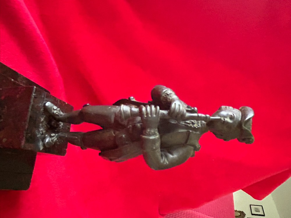 A 19th-century cast bronze statuette depicting a male piper in 18th-century attire standing on a tiered red marble plinth. View VII
