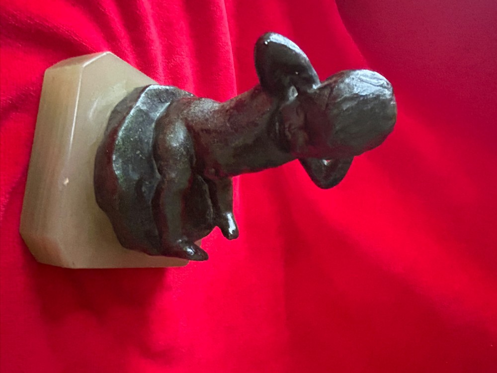 A patinated bronze figurine depicting a seated baby stretching with hands behind its head, mounted on a chamfered pale onyx base. View VI
