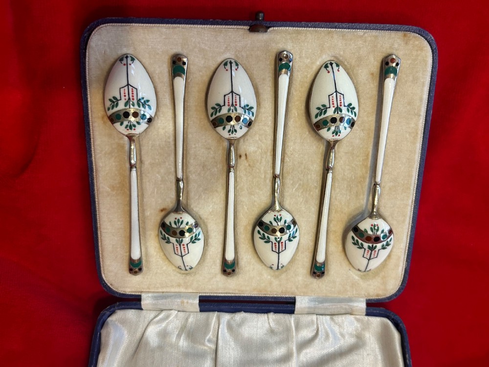 A cased set of six George V sterling silver coffee spoons with white, green, and red enamel decoration in a velvet-lined fitted box.