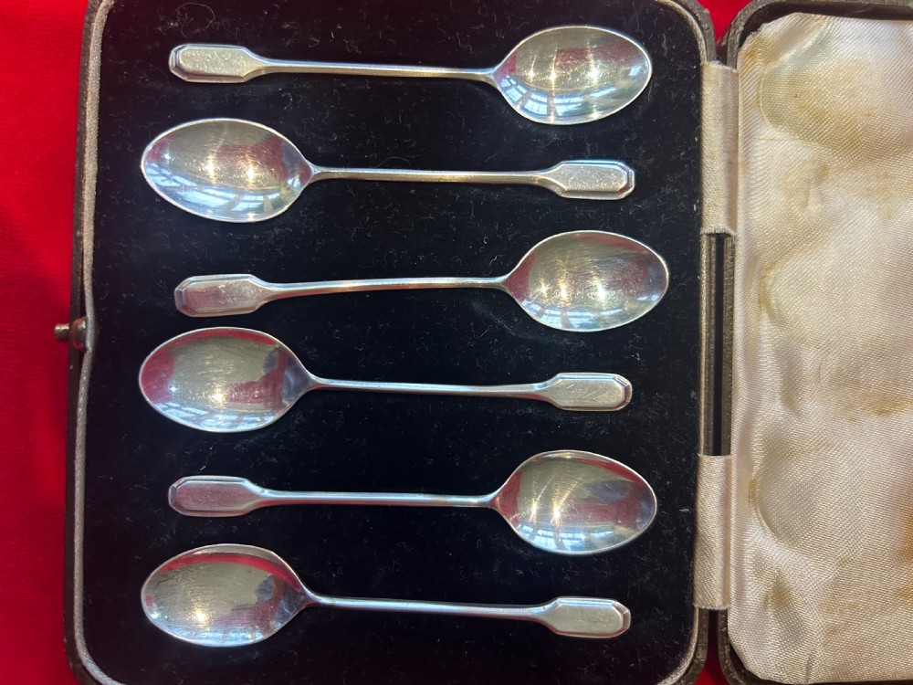 A set of six silver coffee spoons with simple geometric stems resting inside a black velvet and white satin lined presentation case. View II