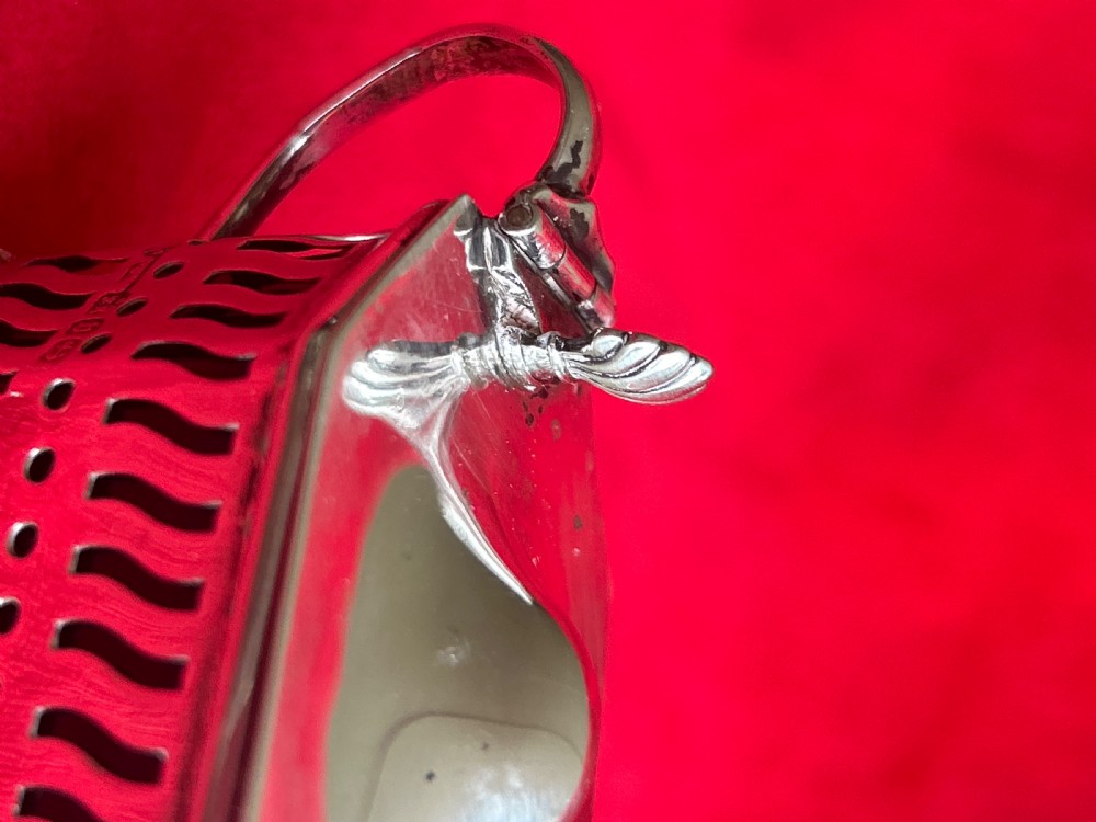 A pierced silver mustard pot featuring a hinged lid with thumbpiece, scroll handle, and small ball feet. View V