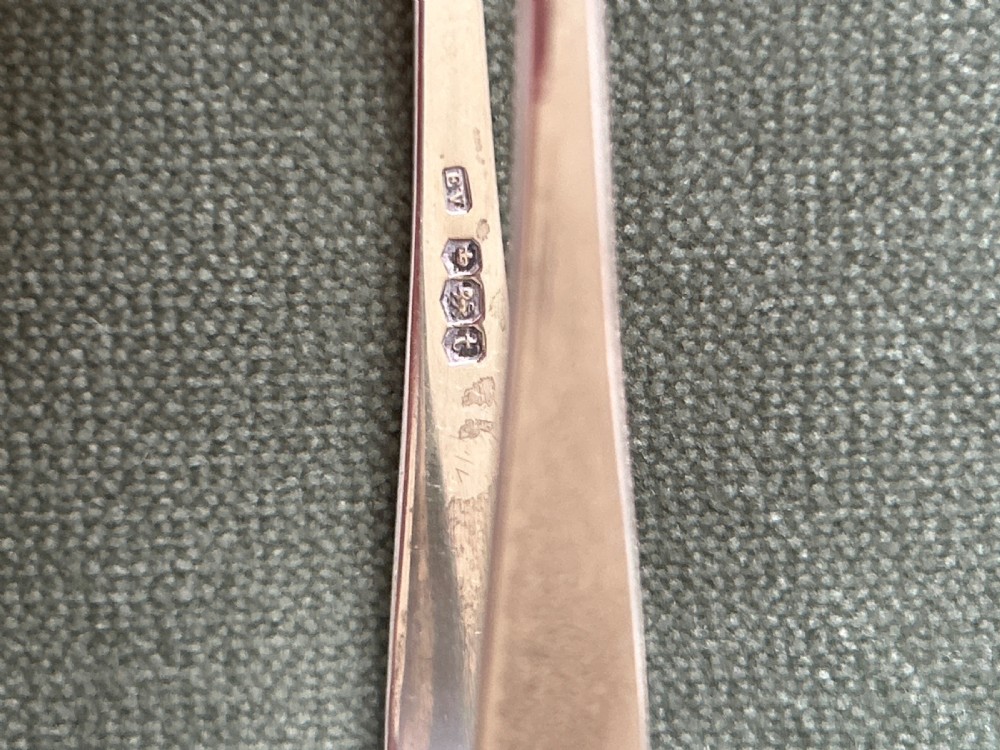 A pair of polished silver sugar tongs with spoon-shaped grips placed on a green fabric surface. View IV