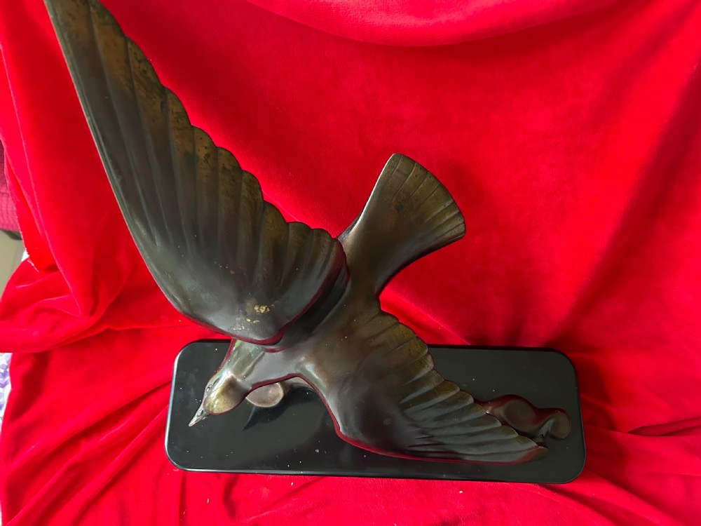 A French Art Deco dark bronze sculpture depicting a stylized bird with outstretched wings in flight mounted on a black rectangular marble base.