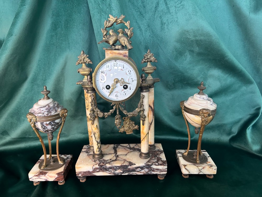 A French late 19th-century clock garniture in veined cream marble and gilt metal featuring a columned clock flanked by two matching cassolette urns.