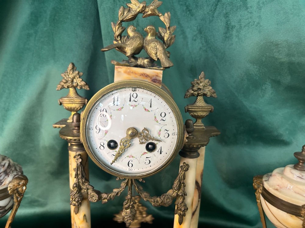 A French late 19th-century clock garniture in veined cream marble and gilt metal featuring a columned clock flanked by two matching cassolette urns. View II