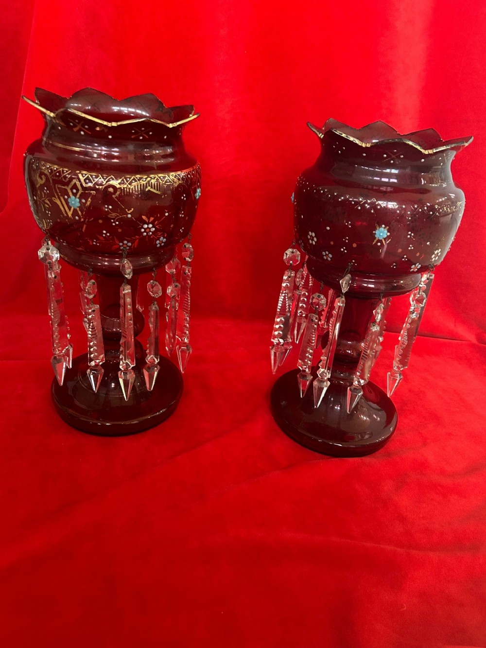 A pair of Victorian ruby glass mantel lustres featuring scalloped edges, hand-painted floral enamel, gilding, and suspended cut crystal prisms.
