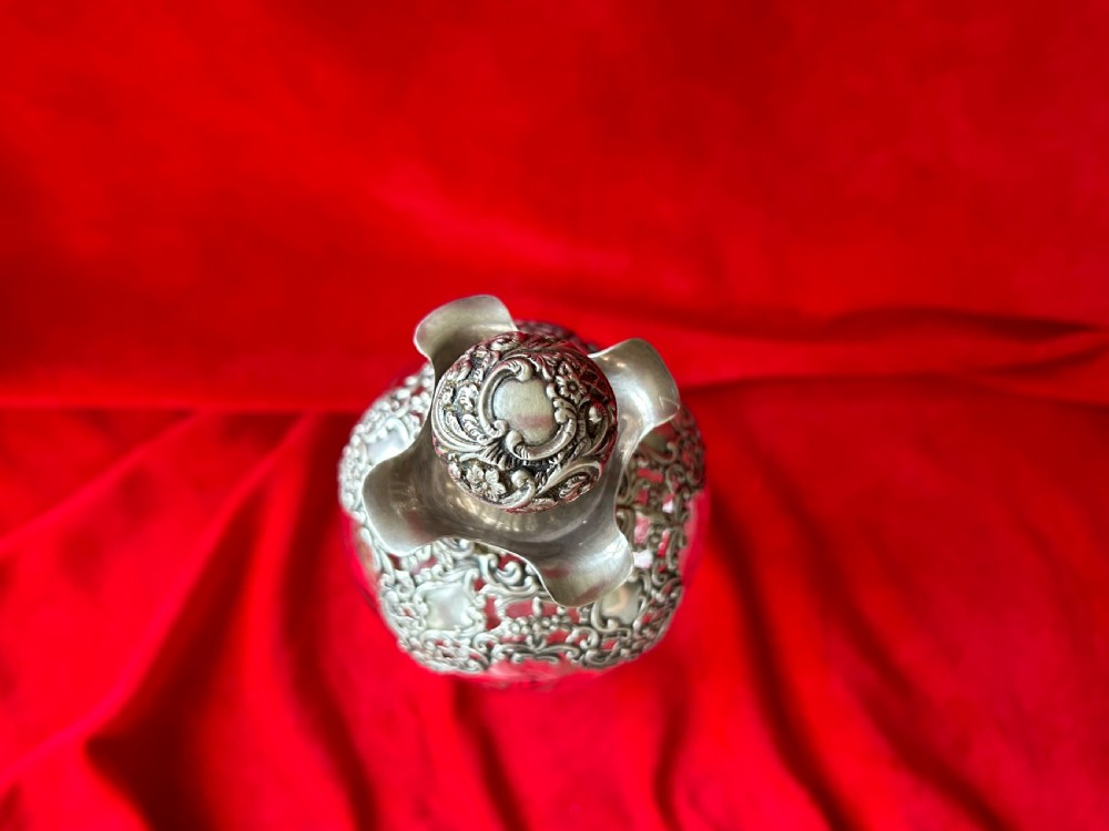 An Edwardian clear glass decanter featuring a pinched waist, decorative pierced silver overlay around the shoulder, and an ornate silver stopper. View II