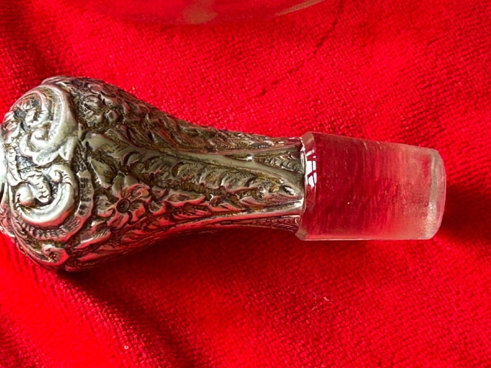 An Edwardian clear glass decanter featuring a pinched waist, decorative pierced silver overlay around the shoulder, and an ornate silver stopper. View IV