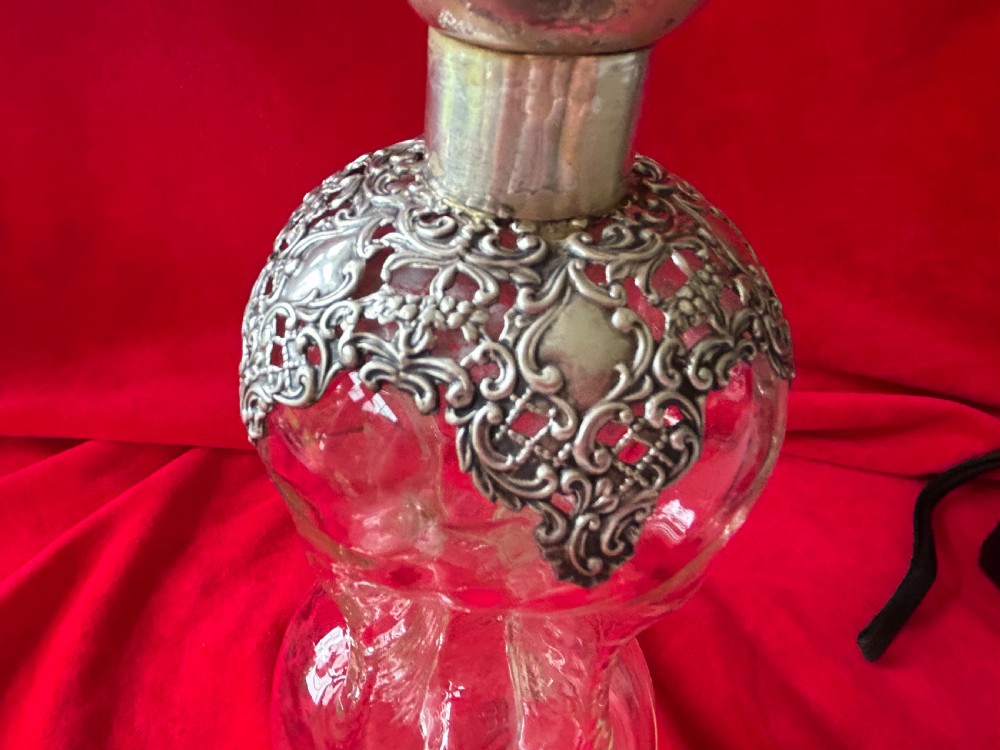An Edwardian clear glass decanter featuring a pinched waist, decorative pierced silver overlay around the shoulder, and an ornate silver stopper. View VII