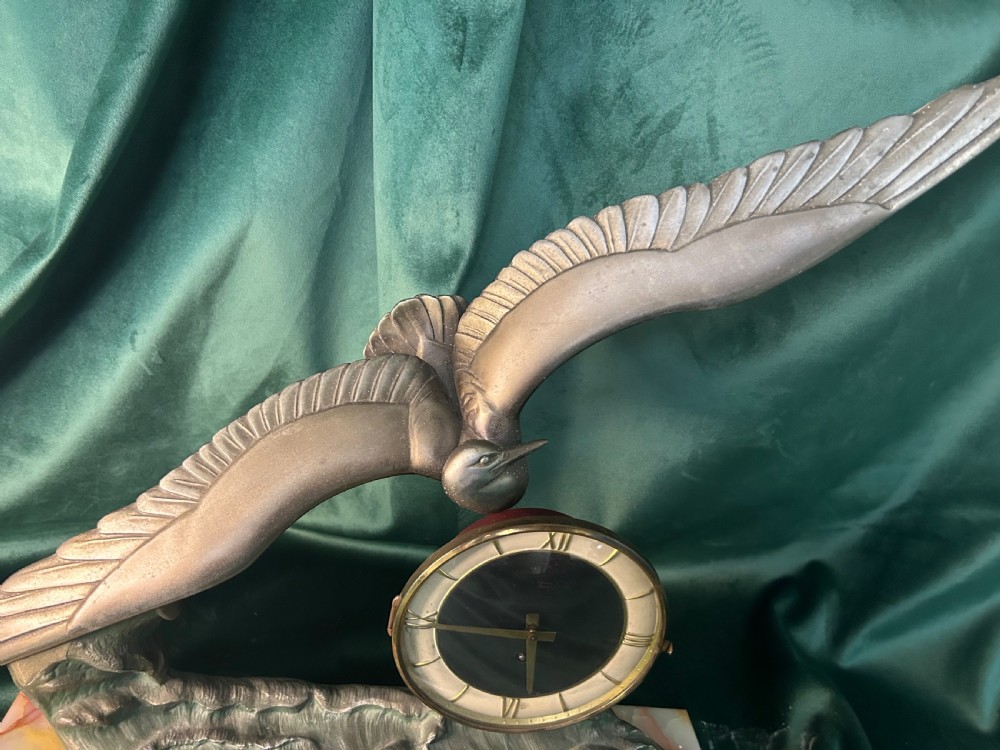 An Art Deco mantel clock featuring a metal bird figure in flight over waves beside a round dial on an onyx plinth. View III