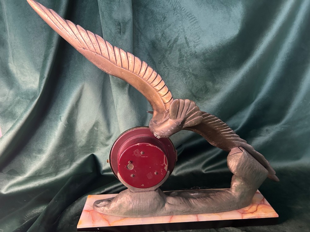 An Art Deco mantel clock featuring a metal bird figure in flight over waves beside a round dial on an onyx plinth. View IV