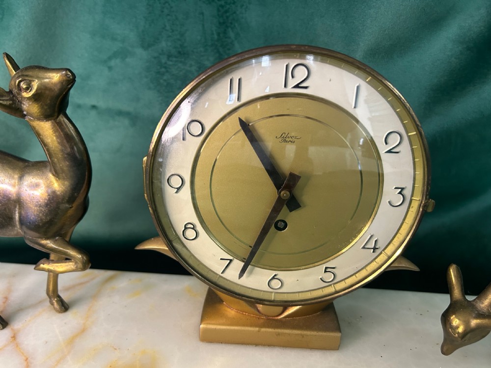 An Art Deco circular brass clock signed Silvoz Paris featuring Arabic numerals on a gold-toned face mounted on a rectangular base.