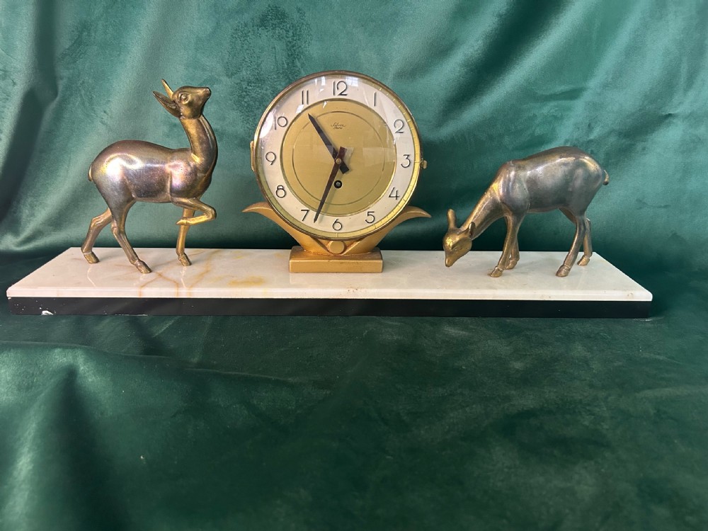 An Art Deco circular brass clock signed Silvoz Paris featuring Arabic numerals on a gold-toned face mounted on a rectangular base. View II