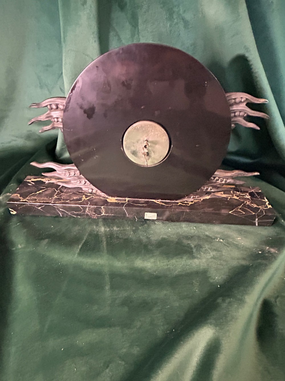An Art Deco mantel clock featuring a circular cream alabaster dial with black circular hour markers, set upon a black veined marble base with silver-toned metal winged accents. View III