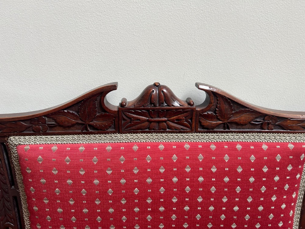 A Victorian mahogany settee featuring carved crest rails, twin padded back cushions in red patterned fabric, turned legs on castors, and a wide upholstered seat. View II