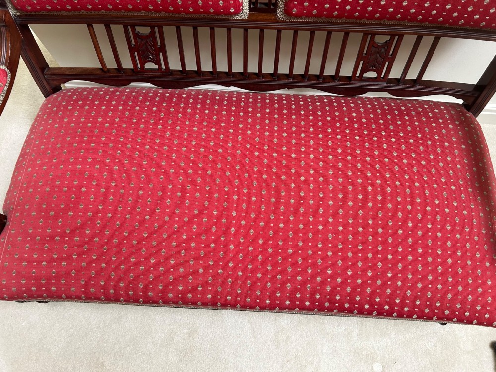 A Victorian mahogany settee featuring carved crest rails, twin padded back cushions in red patterned fabric, turned legs on castors, and a wide upholstered seat. View III