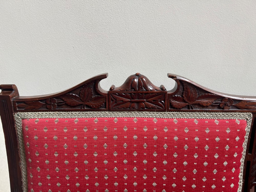 A Victorian mahogany settee featuring carved crest rails, twin padded back cushions in red patterned fabric, turned legs on castors, and a wide upholstered seat. View VI