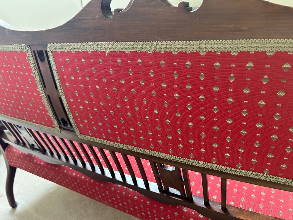 A Victorian mahogany settee featuring carved crest rails, twin padded back cushions in red patterned fabric, turned legs on castors, and a wide upholstered seat. View VII