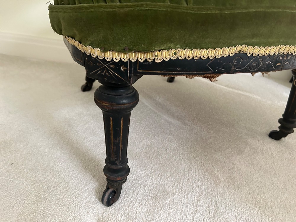 A Victorian ebonised wood tub armchair featuring olive green velvet upholstery, a padded horseshoe backrest supported by turned spindles, and gold braided trim. View II
