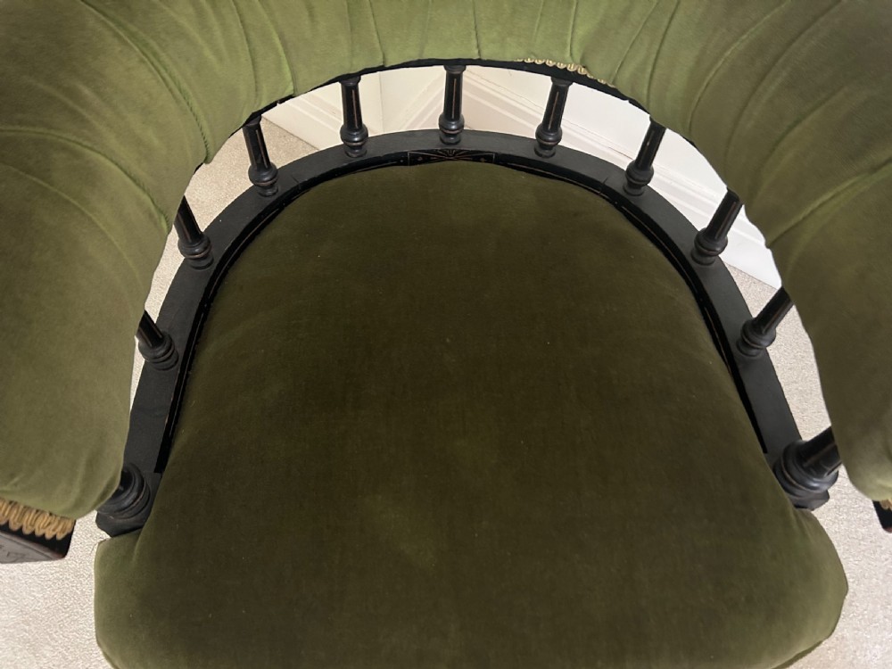 A Victorian ebonised wood tub armchair featuring olive green velvet upholstery, a padded horseshoe backrest supported by turned spindles, and gold braided trim. View III