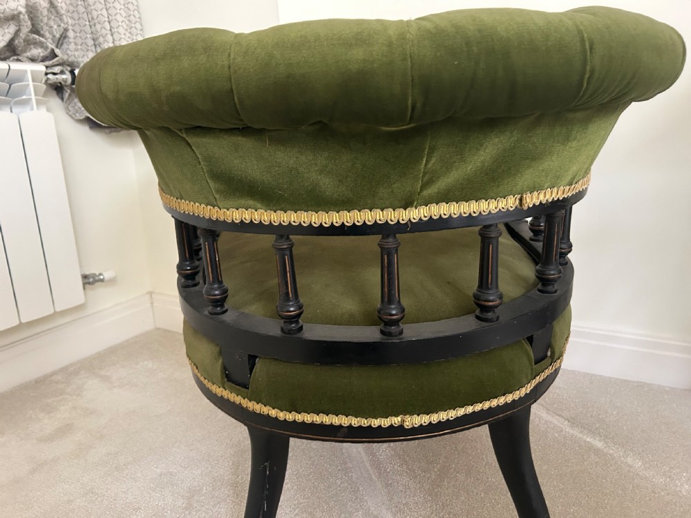 A Victorian ebonised wood tub armchair featuring olive green velvet upholstery, a padded horseshoe backrest supported by turned spindles, and gold braided trim. View V