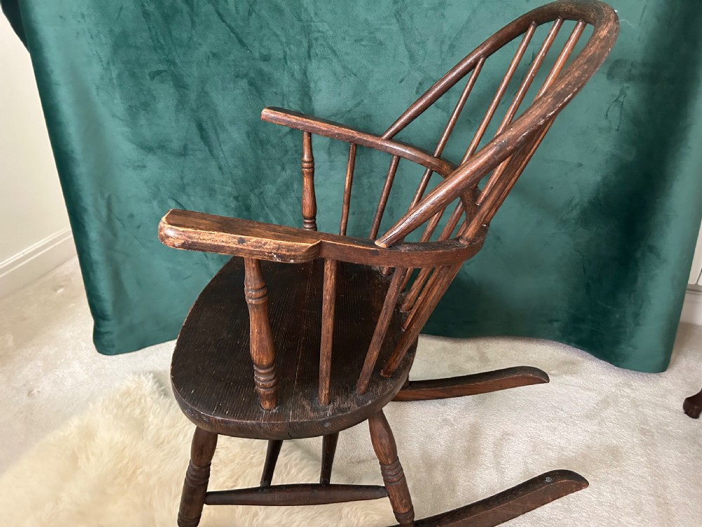 A dark stained wooden Windsor rocking chair featuring a spindle hoop back, curved armrests, turned legs, and wooden runners. View III