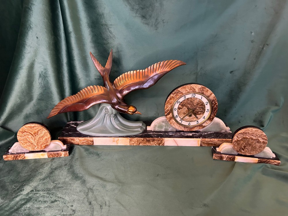 A French Art Deco three-piece clock garniture made of variegated brown marble and pale onyx, featuring a central spelter bird sculpture alongside a round clock face.