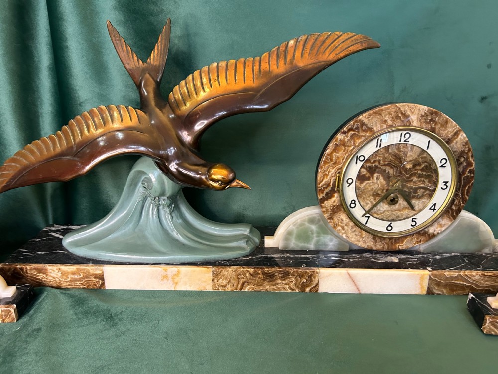 A French Art Deco three-piece clock garniture made of variegated brown marble and pale onyx, featuring a central spelter bird sculpture alongside a round clock face. View II