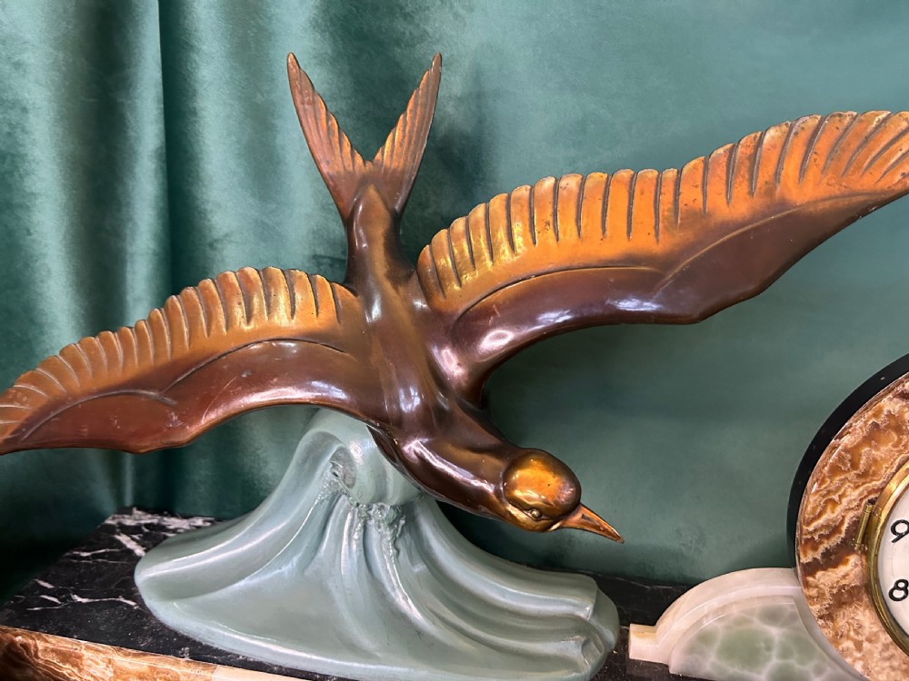 A French Art Deco three-piece clock garniture made of variegated brown marble and pale onyx, featuring a central spelter bird sculpture alongside a round clock face. View IV