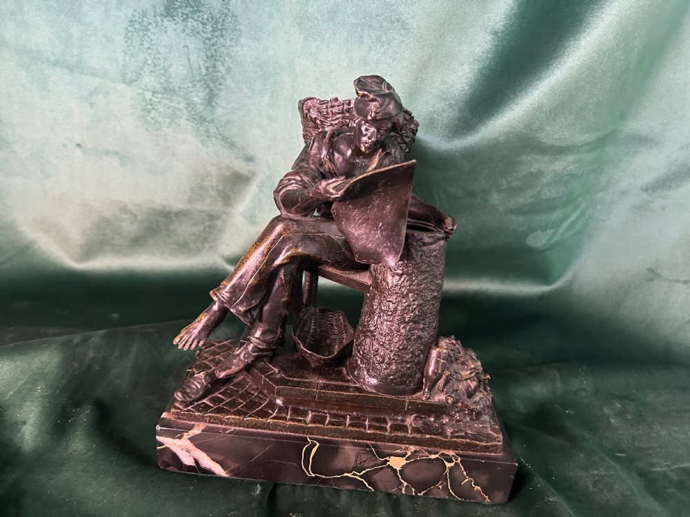 A patinated dark bronze sculpture depicting a seated man reading a newspaper, mounted on a black veined marble base.