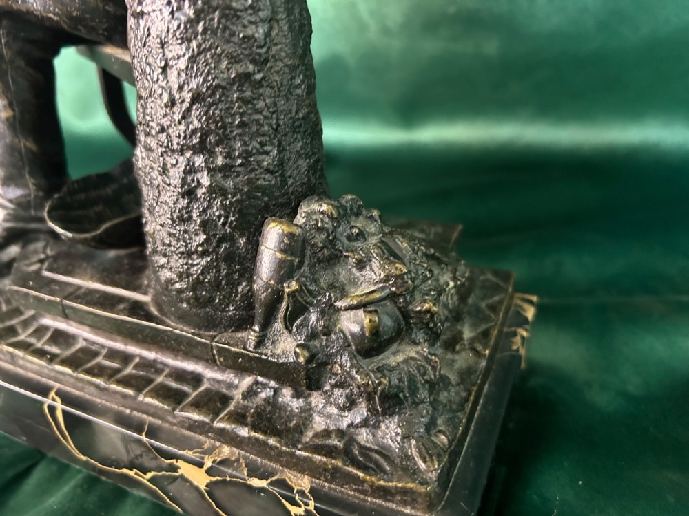 A patinated dark bronze sculpture depicting a seated man reading a newspaper, mounted on a black veined marble base. View II