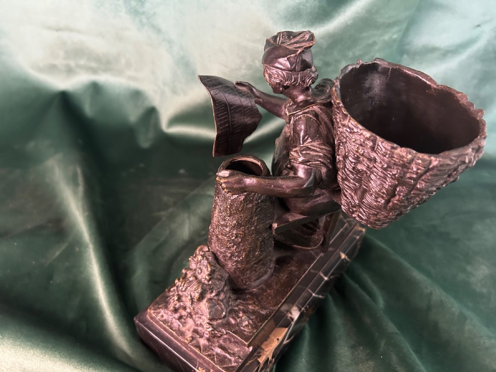 A patinated dark bronze sculpture depicting a seated man reading a newspaper, mounted on a black veined marble base. View V