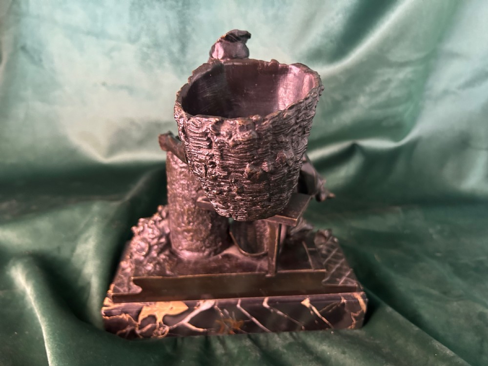 A patinated dark bronze sculpture depicting a seated man reading a newspaper, mounted on a black veined marble base. View VI