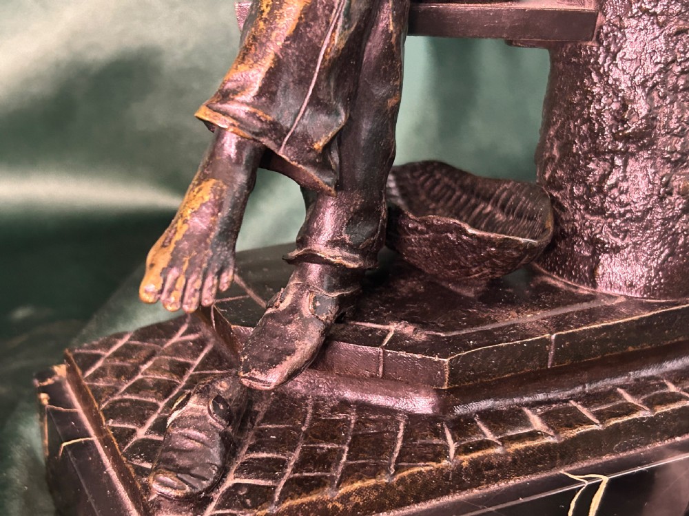 A patinated dark bronze sculpture depicting a seated man reading a newspaper, mounted on a black veined marble base. View VIII