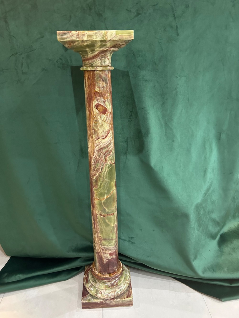 A tall variegated green onyx column pedestal featuring a square moulded top capital and a stepped square base.
