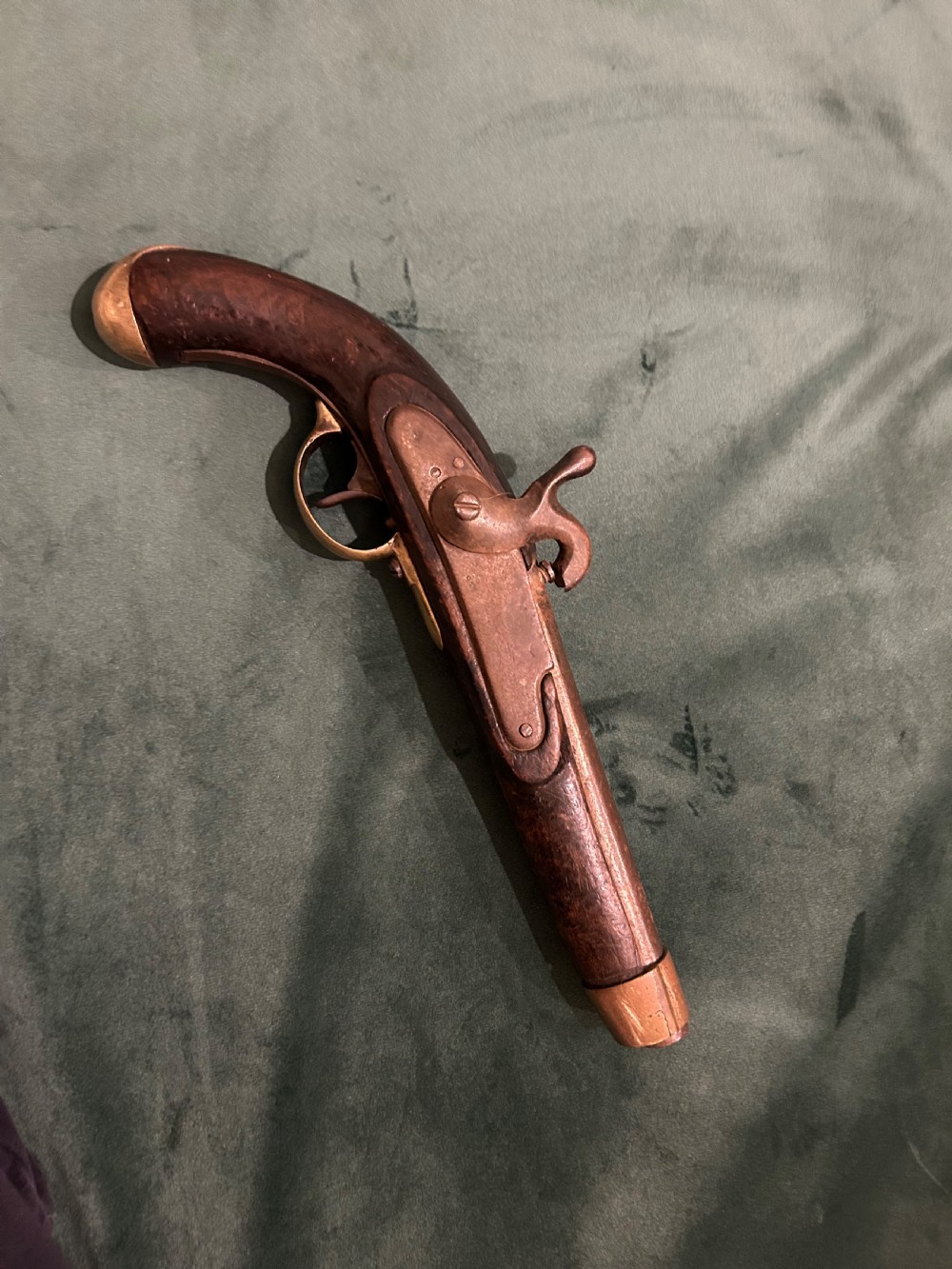An antique single-barrel percussion pistol featuring a carved walnut stock, a metal hammer mechanism, and brass fittings along the trigger guard and butt cap.