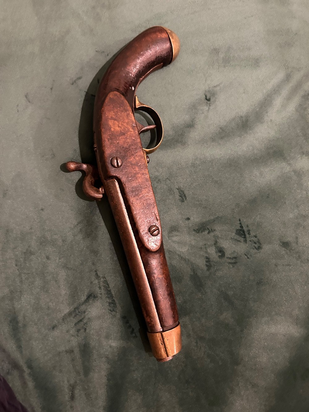 An antique single-barrel percussion pistol featuring a carved walnut stock, a metal hammer mechanism, and brass fittings along the trigger guard and butt cap. View III